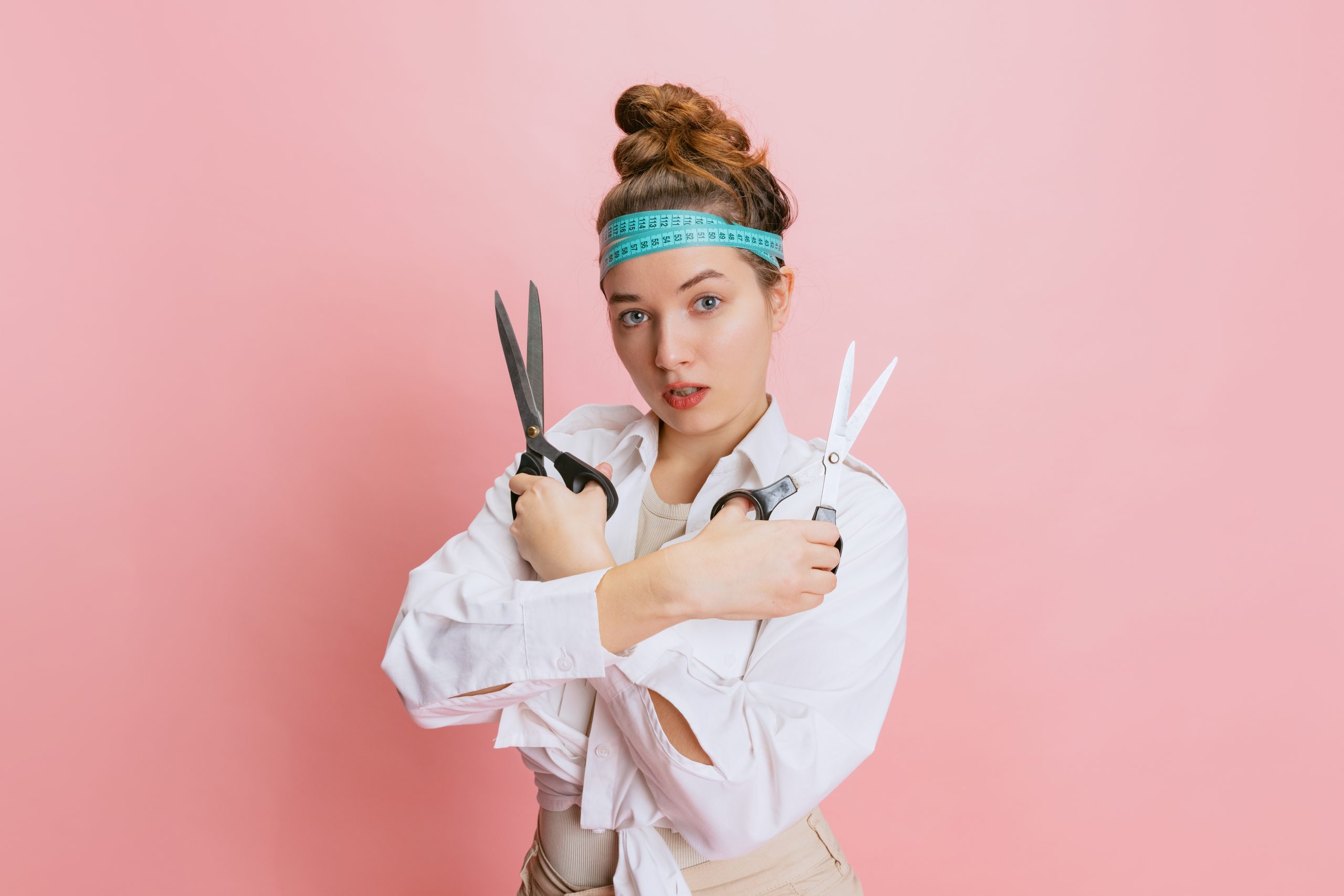 Cropped portrait of young seamstress with scissors posing isolated over pink studio background